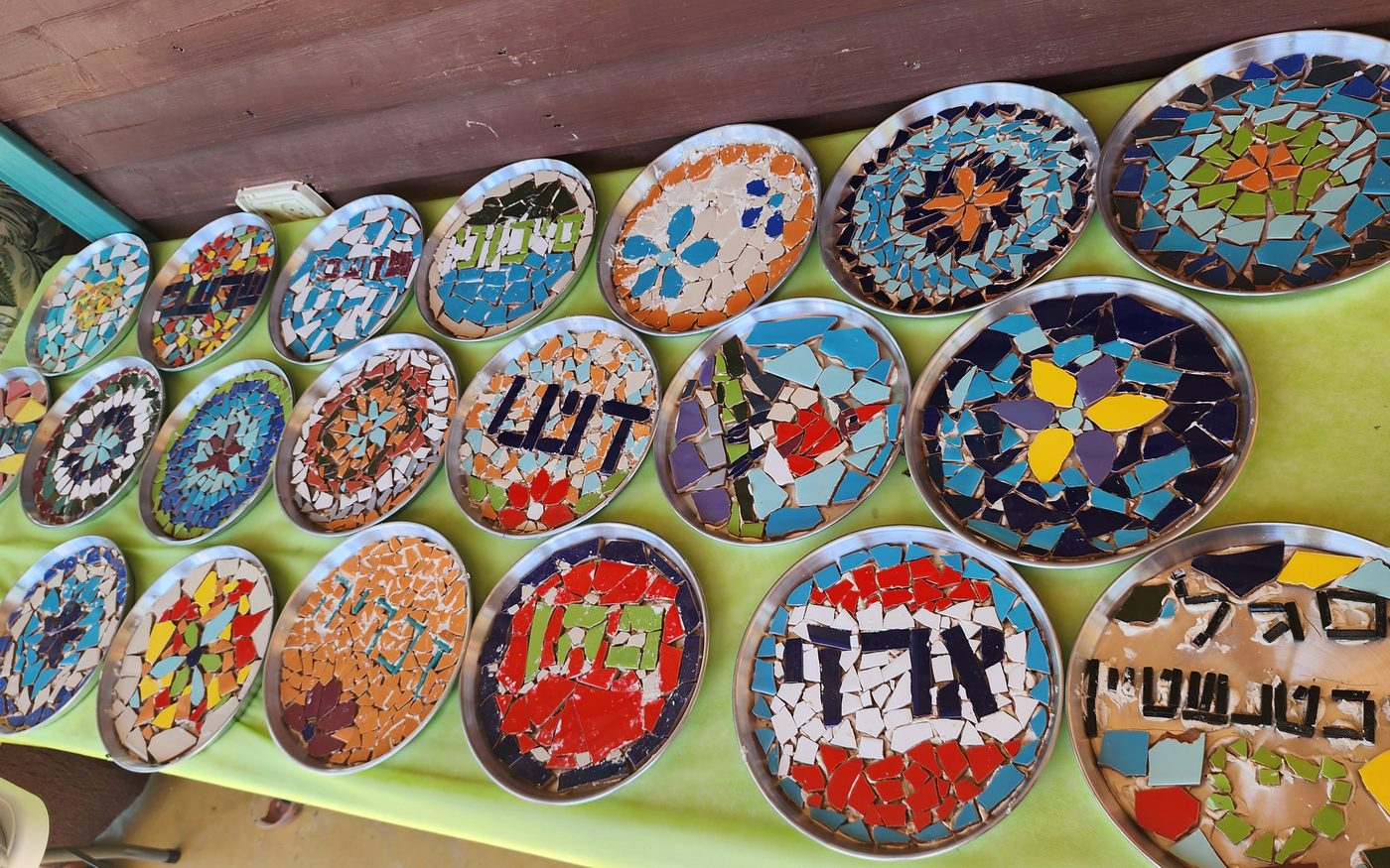 שולחן מלא במגשי פסיפס גמורים, עם שמות ודוגמאות של המשתתפים